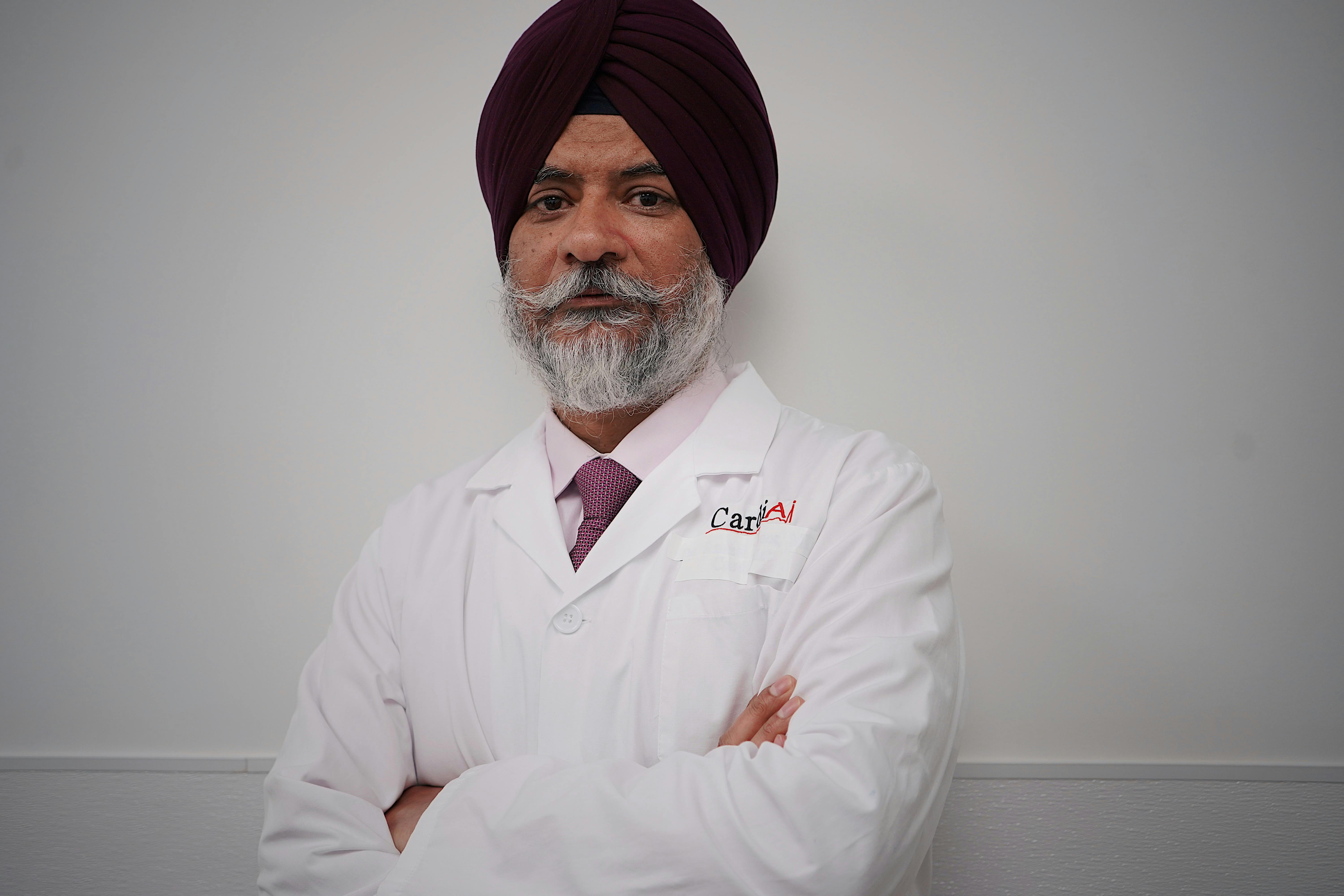 Portrait of a confident doctor standing with arms crossed, wearing a white coat and turban.