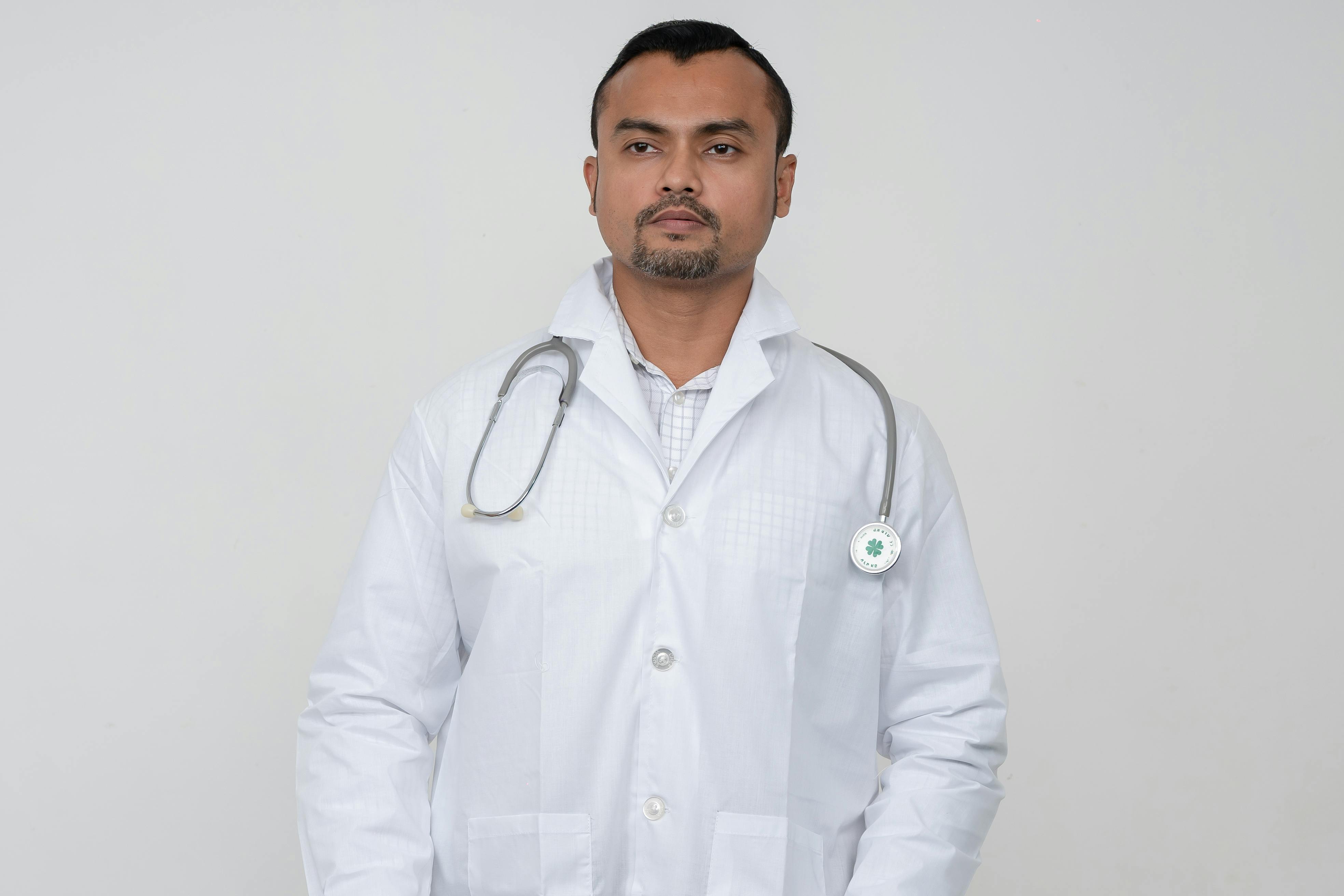 A professional portrait of a South Asian male doctor in a white coat with a stethoscope.