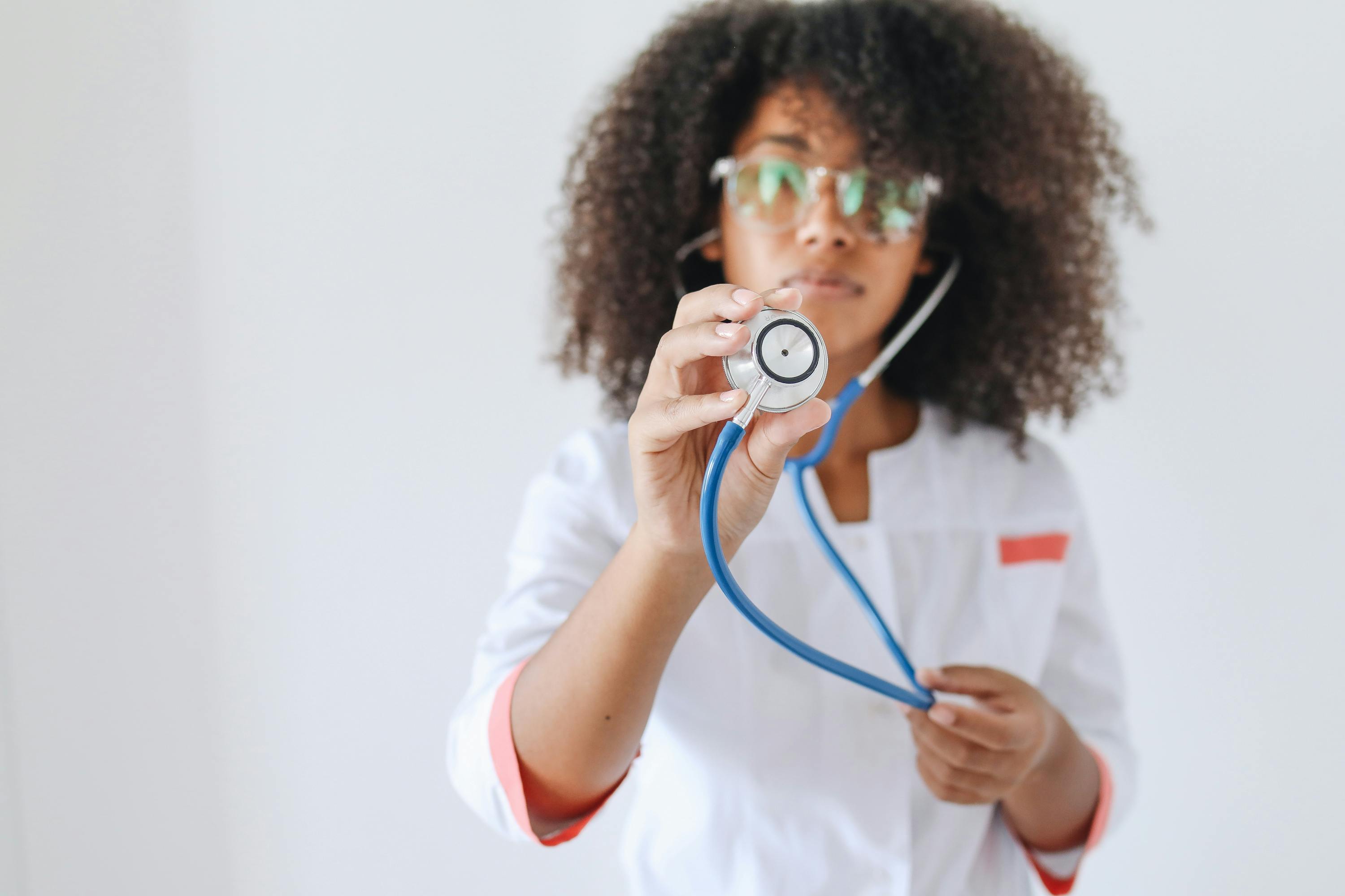 African American female doctor holding a stethoscope against a white background.