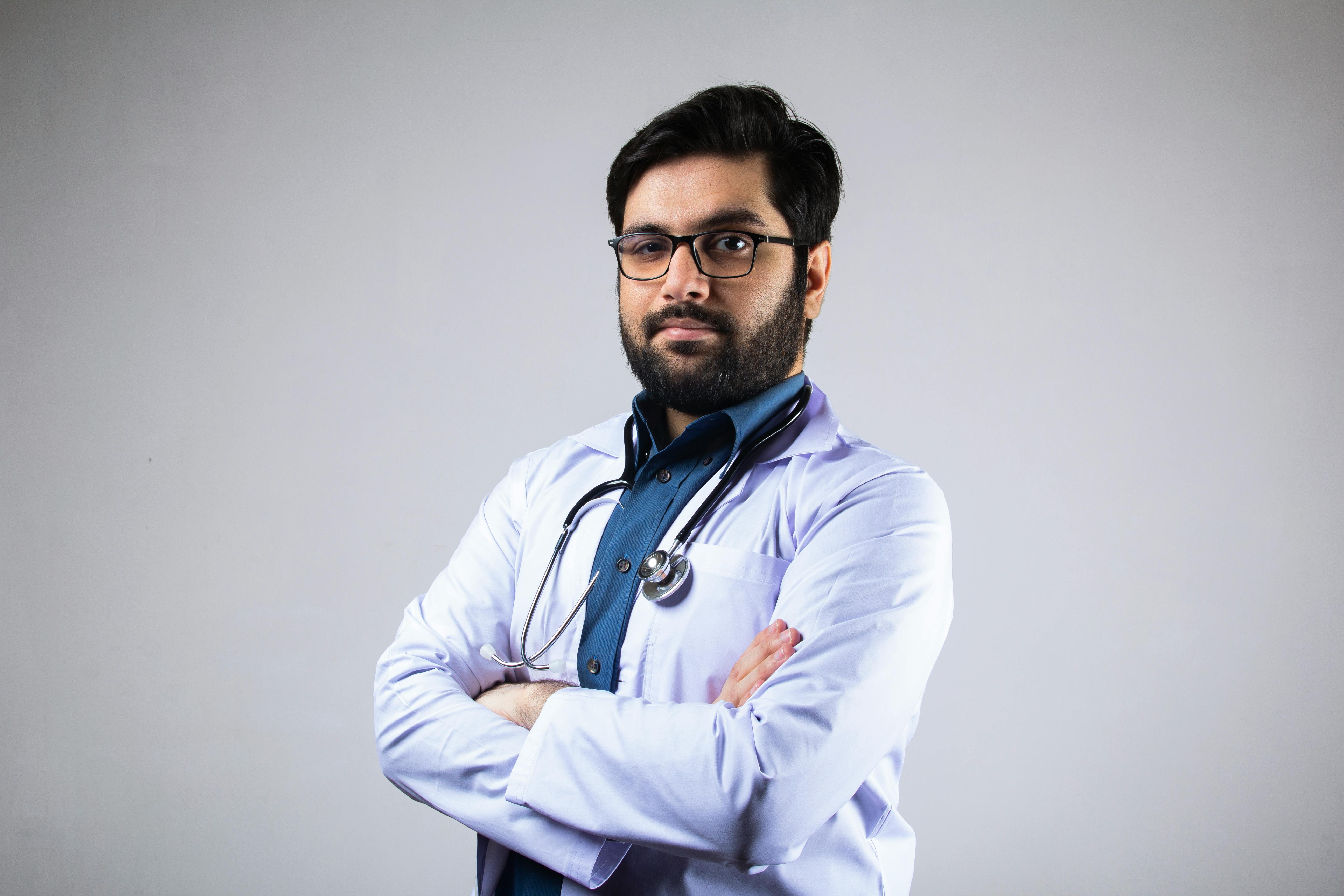 Portrait of a serious male doctor in a white coat with a stethoscope, arms crossed, studio background.